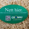 Ovaler, grüner Aufkleber mit der Aufschrift "Nett hier, aber warst du schon mal in Gronaui im Münsterland?", einen QR-Code und dem Logo des Stadtmarketings Gronau. Im Hintergrund ist Stroh zu sehen.
