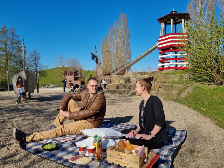 Zwei Personen genießen ein Picknick auf dem Piratenspielplatz auf dem Inselparkgelände in Gronau