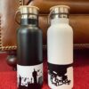 Eine schwarze Gronau Trinklasche mit weißem Motiv und eine weiße Gronau-Trinkflasche mit schwarzem Motiv nebeneinander auf einem roten Untergrund.