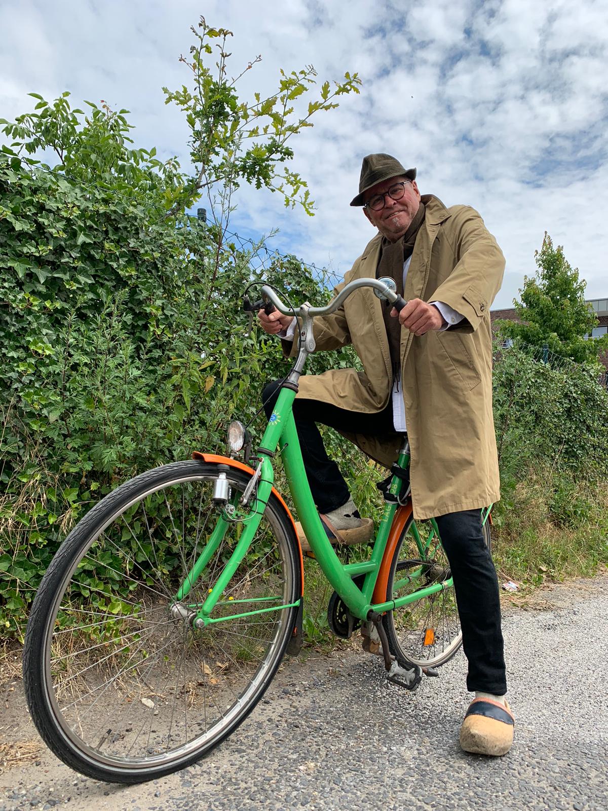 Ein Mann auf einem grünen Fahrrad vor einer Hecke.