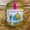 Ein Glas Honig von der Imkerei Schatz in Gronau mit der Aufschrift "Sommerblütenhonig". Auf dem Etikett ist eine Biene und ein Bienenstock zu sehen.