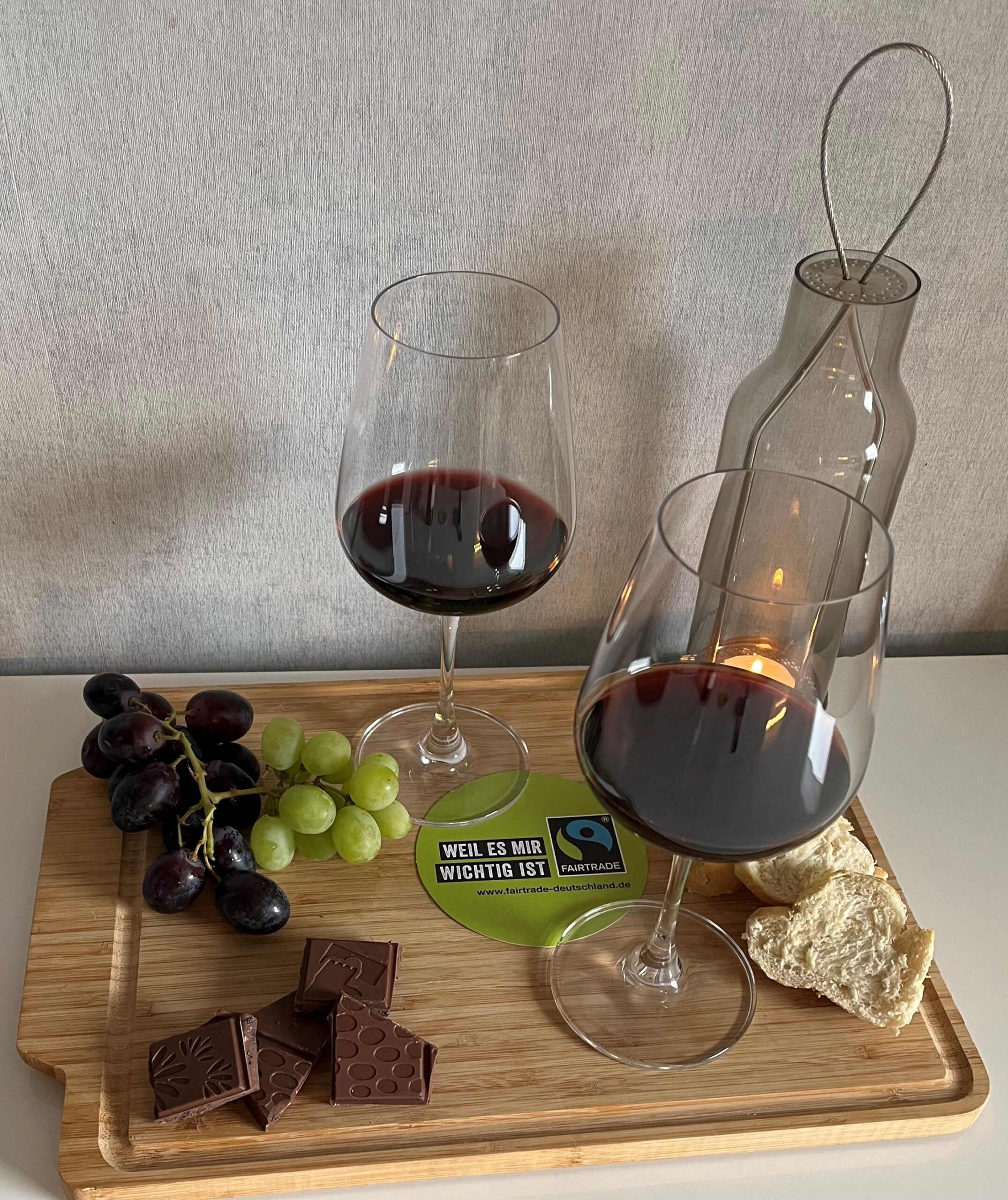 Zwei Gläser Wein, rote und grüne Weintrauben, Schokolade und Brot - auf einem Schneidebrettchen serviert