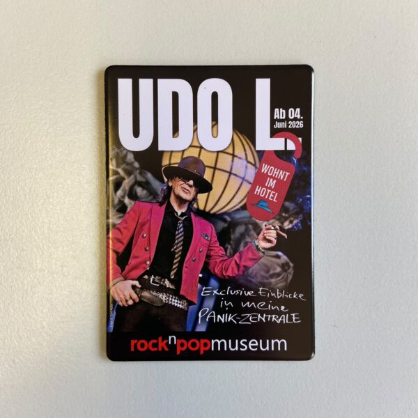 Nahaufnahme desselben Magneten, freistehend auf hellem Untergrund. Zu sehen ist das Ausstellungsmotiv „UDO L." mit Udo Lindenberg im roten Jackett, schwarzem Hut und Sonnenbrille vor einer goldenen Diskokugel, in der Hand eine rauchende Zigarre. Ein rotes „Bitte nicht stören"-Türschild mit der Aufschrift „Wohnt im Hotel" hängt neben ihm. Unten der Schriftzug „rock'n'popmuseum".