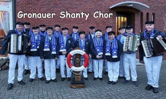 Op de foto is het shantykoor te zien in een uniforme kleding. Ze dragen allemaal een witte broek en een blauw bovenstuk.