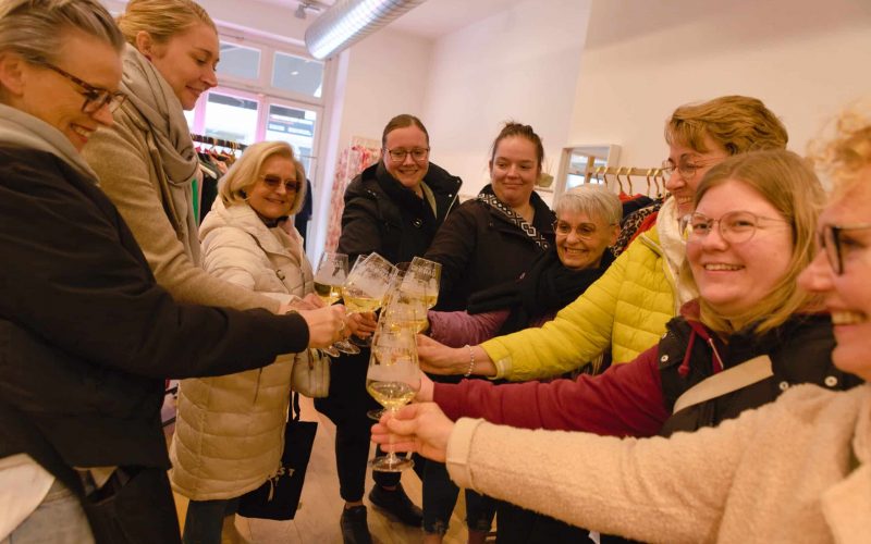 Eine Gruppe Personen stößt in der Mitte mit Weingläsern an.