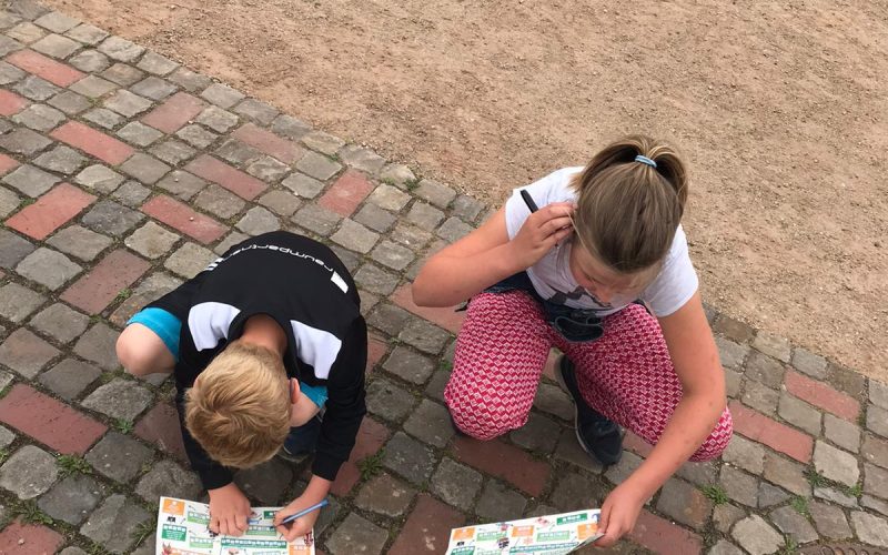 Op de foto zijn twee kinderen te zien die een kinderrally op de grond invullen.